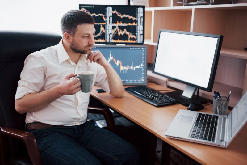 young businessman is sitting office table working computer with many monitors diagrams monitor stock broker analyzes binary options charts hipster man drinking coffee studying 146671 15040 Cronos Asia